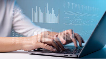 Close up of businesswoman hands typing on laptop keyboard with graphs and diagramsの素材