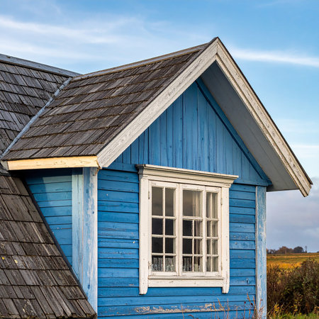 Old wooden house with blue shingles and a white window.の素材
