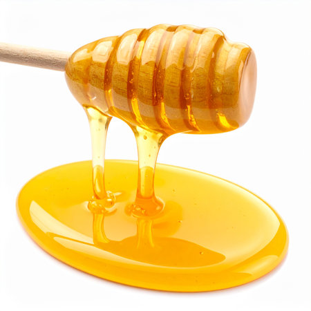 Honey dripping from a wooden honey dipper isolated on white backgroundの素材