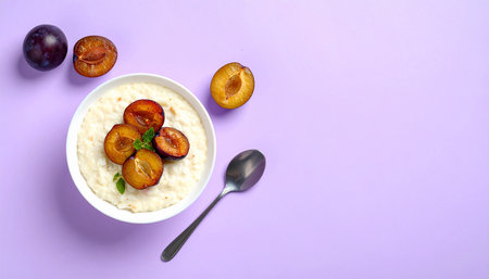Oatmeal porridge with plums in a bowl on a purple background, top view, copy spaceの素材