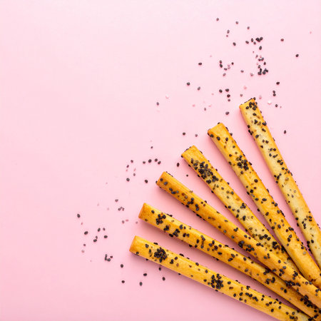 Crispy breadsticks with poppy seeds on a pink background.の素材