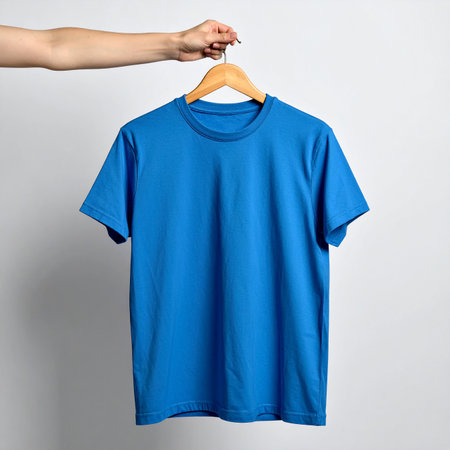 Female hand holding blue t-shirt on hanger on grey backgroundの素材