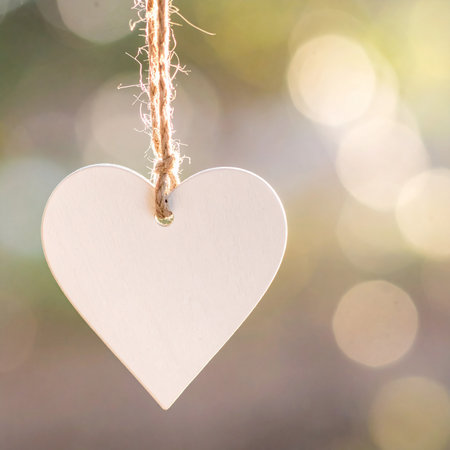 A pale pink heart-shaped tag hangs from twine with a soft, blurred bokeh background.の素材