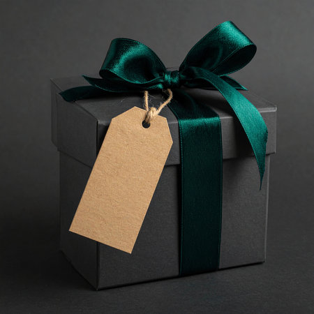 A square dark grey gift box adorned with an emerald green satin ribbon and a kraft paper tag.の素材