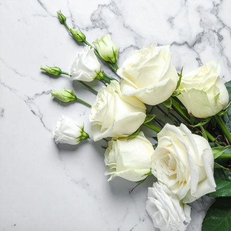 White roses and buds with green leaves arranged on a white marble surface. Clear details and vibrant colors e...の素材