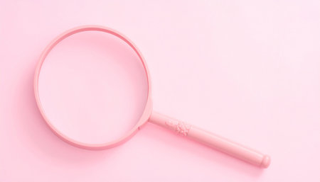 A pink magnifying glass with an ornate handle is placed on a pink surface. Clear details and vibrant colors e...の素材