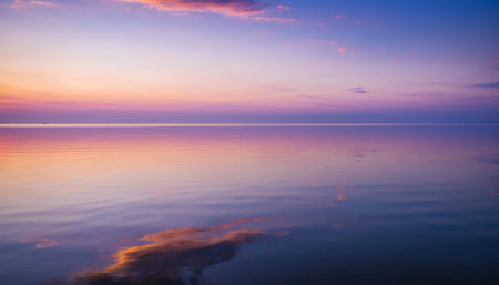 A serene sunset sky with soft pink, purple, and blue hues is reflected on the calm surface of the water.の素材