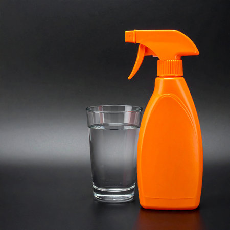 Orange spray bottle and glass of clear liquid on a dark surface. Clear details and vibrant colors enhance vis...の素材