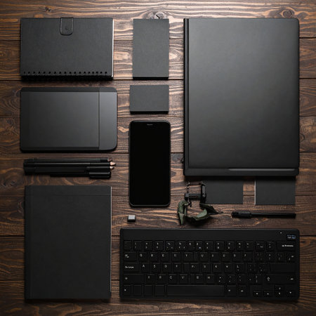 Black stationery and technology items are neatly arranged on a rustic wooden table.の素材