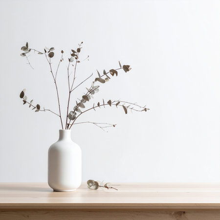 A white vase holds dried eucalyptus branches on a light wooden surface. Clear details and vibrant colors enha...の素材
