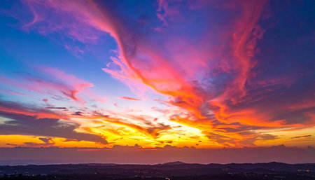 A dramatic sunset sky with swirling pink and orange clouds over a distant landscape.の素材