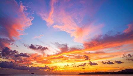 A vibrant sunset over the ocean with dramatic orange and pink clouds and silhouetted islands.の素材