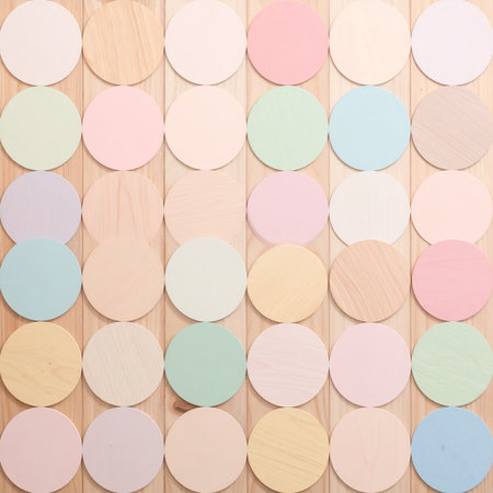 A grid of pastel colored wooden circles arranged on a light wood surface. Clear details and vibrant colors en...の素材