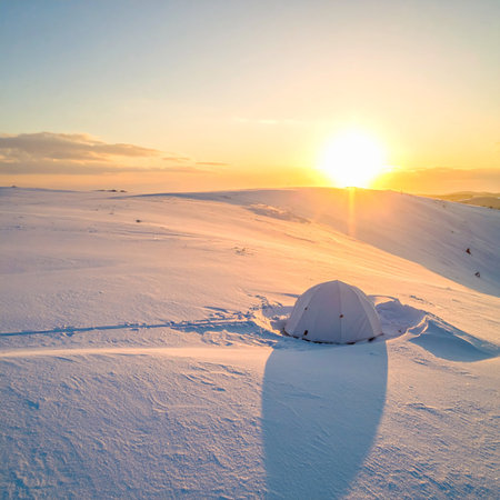A small white dome tent is in a vast snowy landscape during a golden sunset. Clear details and vibrant colors...の素材