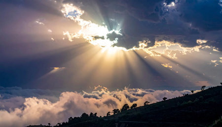 Sunbeams break through clouds over a misty mountain landscape with trees on a hillside.の素材
