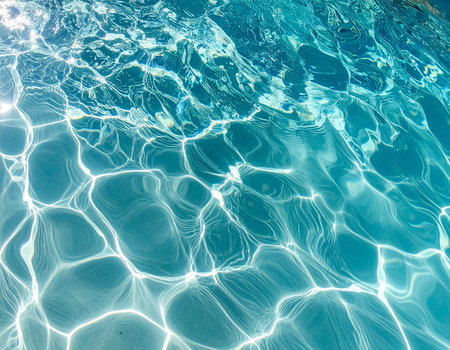 Vibrant blue water surface with intricate patterns of sunlight reflecting and shimmering.の素材