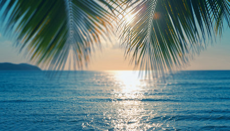 Ocean surface reflects the sun's light, viewed through tropical palm fronds at sunset.の素材