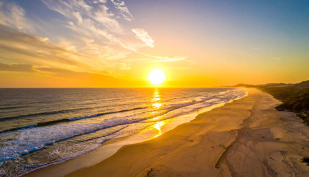 Golden sunset over a tropical beach with gentle waves and distant hills. Clear details and vibrant colors enh...の素材