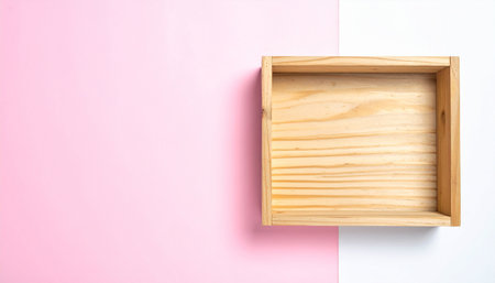 An empty light wood crate sits on a surface split between pink and white with a soft shadow.の素材