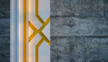 Geometric white and yellow architectural detail contrasts with a textured concrete wall.の素材