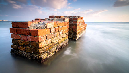 Two weathered brick structures stand partially submerged in the ocean with smooth, flowing waves.の素材
