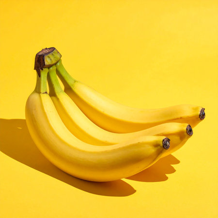 Three ripe yellow bananas are positioned on a vibrant yellow background, with a noticeable shadow.の素材