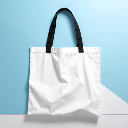 A white fabric tote bag with black straps is centered on a blue and white diagonal background.の素材