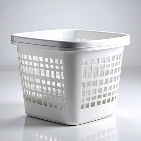 A white plastic laundry basket with square perforations sits on a white surface. Clear details and vibrant co...の素材