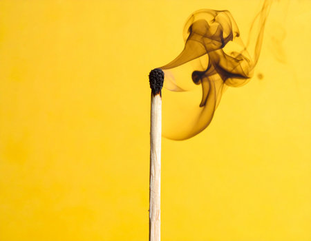 A smoldering matchstick with dark smoke swirling against a bright yellow background.の素材