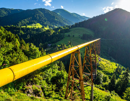 A bright yellow pipeline stretches across a verdant mountain landscape under a clear blue sky.の素材