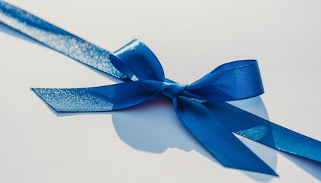 A close-up of a blue ribbon tied into a bow on a white surface with shadows. Clear details and vibrant colors...の素材