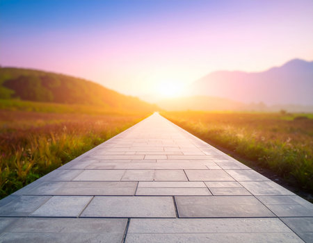 A stone pathway stretches towards a vibrant sunset over rolling hills and distant mountains.の素材
