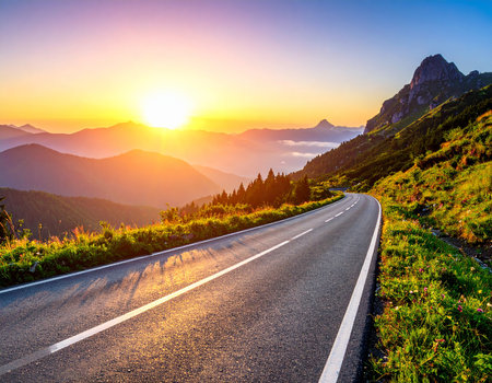 A winding mountain road bathed in the golden light of sunrise with a bright sunburst.の素材