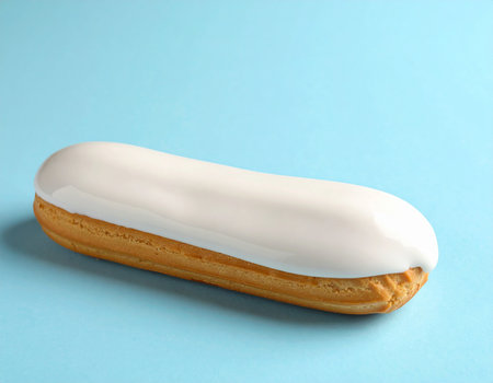 A vanilla glazed eclair pastry is positioned at an angle on a light blue background.の素材