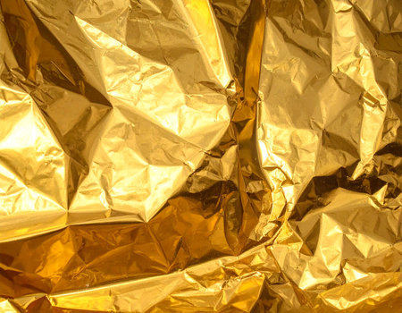 Close-up of crumpled gold foil with bright reflections and deep shadows creating an abstract texture.の素材