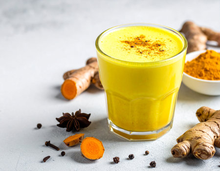 A glass of golden turmeric latte is surrounded by fresh ginger roots, star anise, and turmeric powder.の素材