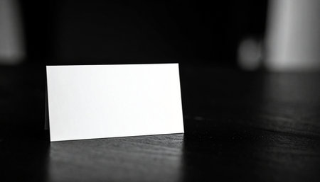 A blank white card rests on a dark textured surface in a black and white studio shotの素材