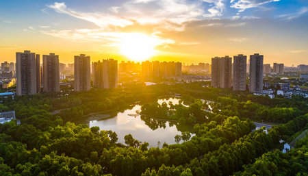 Aerial perspective of an urban park featuring a reflective pond and apartment blocks, bathed in the bright light of a sunset.の素材
