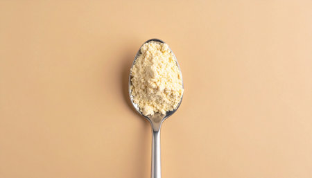 Detailed view of a metal spoon overflowing with fine yellow powder, set against a smooth, light brown background.の素材