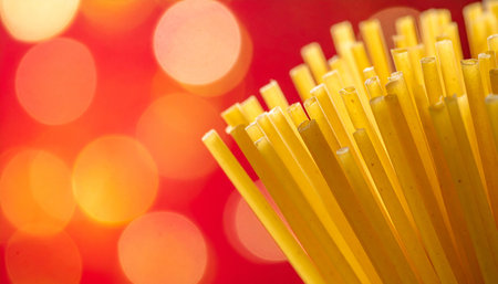 A close-up perspective of uncooked spaghetti pasta strands, set against a red background illuminated by soft, circular bokeh lights.の素材