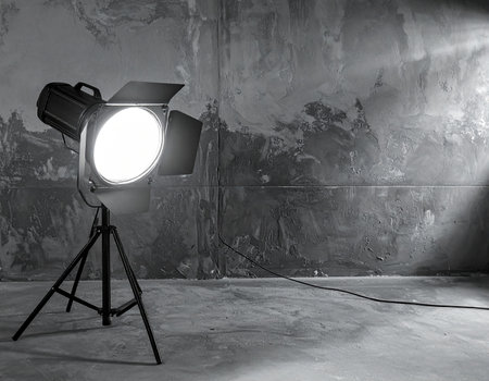 A studio lighting fixture with a bright light shines against a textured wall in an empty room.の素材