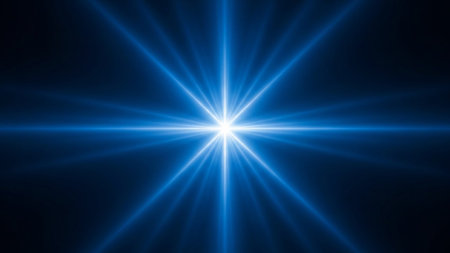 An intense blue starburst emanates bright, radiating light beams from a central point against a dark background.の素材