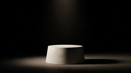 A light beige concrete cylinder pedestal is illuminated by a spotlight against a dark, moody background.の素材
