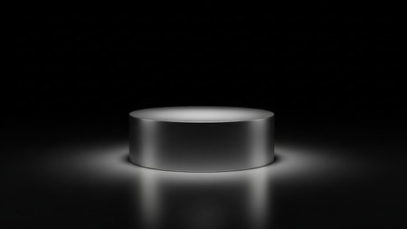 A sleek silver cylindrical display pedestal with subtle spotlight illumination creating soft reflections on a dark surface.の素材