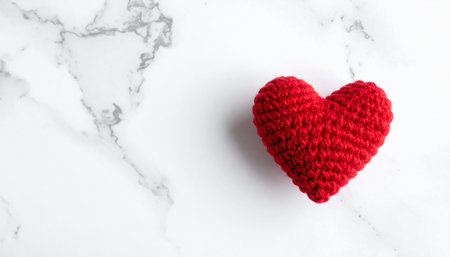 A red crocheted heart is placed on a white marble surface, leaving significant white space on the left.の素材