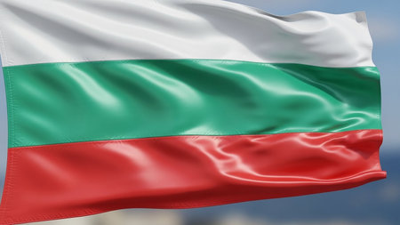 The national flag of Bulgaria, composed of horizontal white, green, and red stripes, waves in the wind against a blurred background of sky and sea.の素材