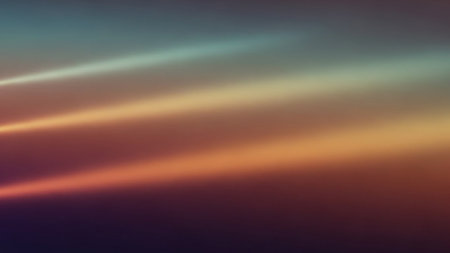 An abstract background features softly blended warm light beams in shades of orange, yellow, and brown against a dark, diffused backdrop.の素材