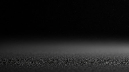 A dark, textured surface with a subtle light gradient and fine dust particles, creating a minimalist and atmospheric background.の素材