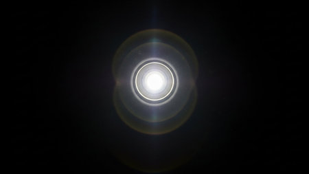 A bright white light source emanates from the center, creating circular lens flares against a dark background.の素材