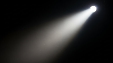 A bright white spotlight beam cuts through the darkness, creating a cone of light and subtle particles.の素材